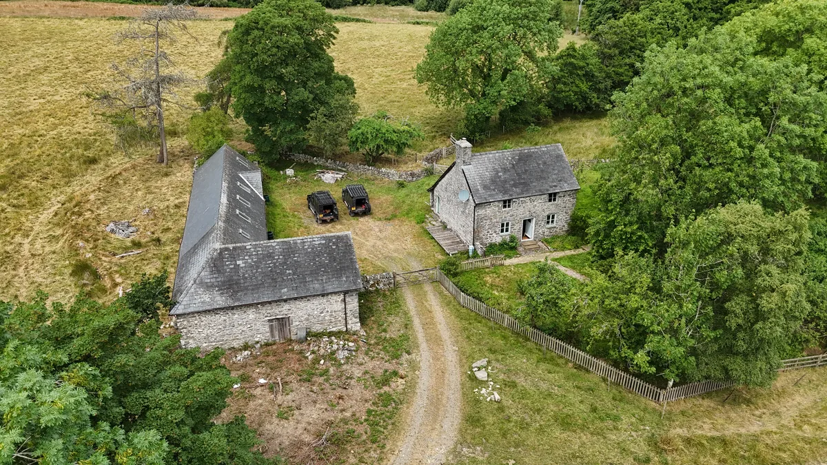 Aerial drone view of a traditional stone cottage and long slate-roofed stone barn in rural border country
